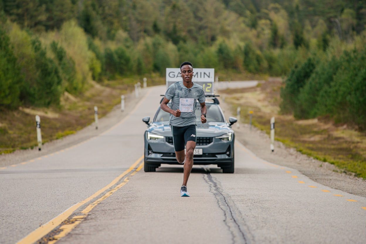 Suldan Hassan running in front of a Polestar 2 on a forest road