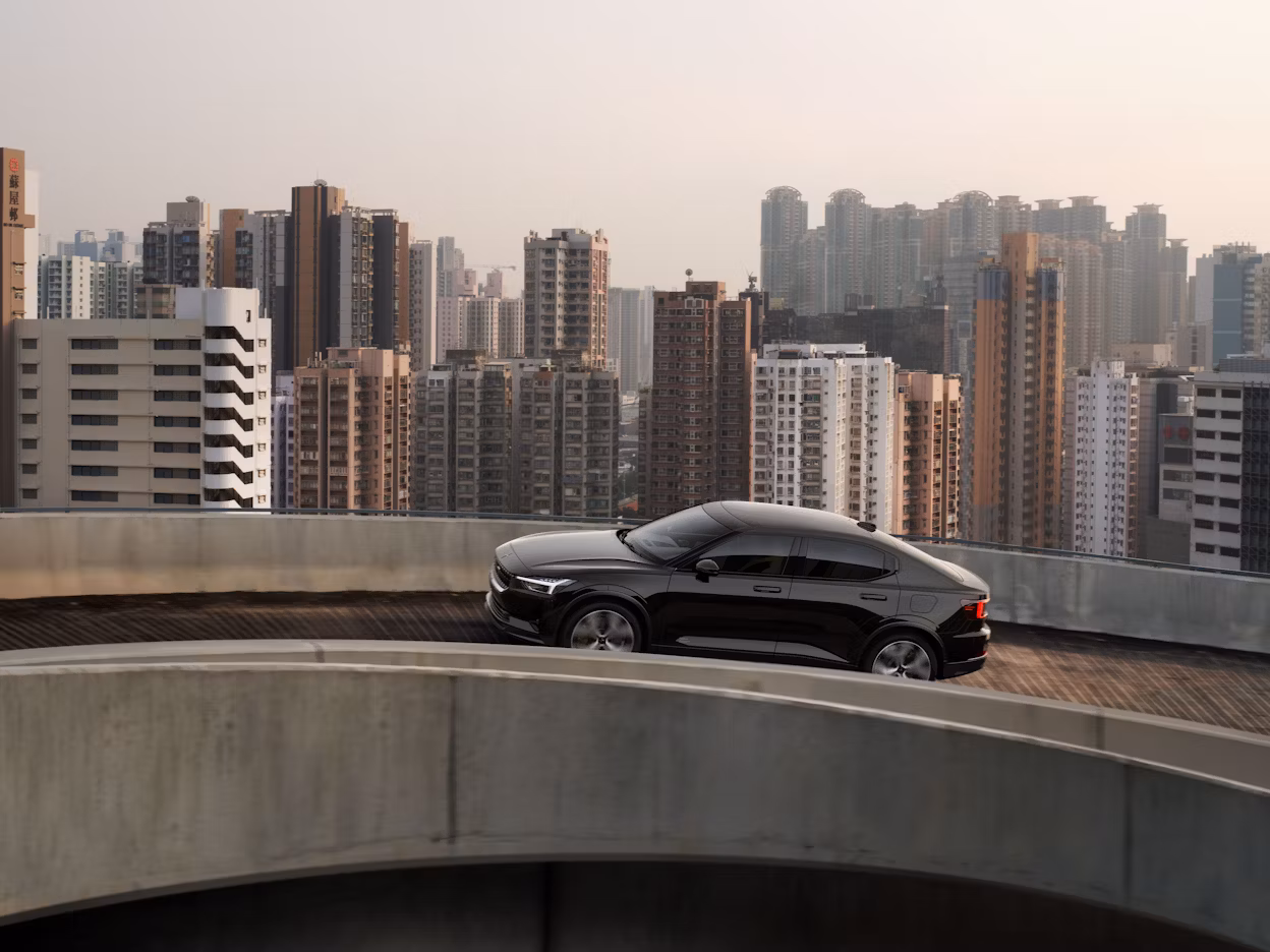 A black Polestar 2 on a road with tall buildings in the background.