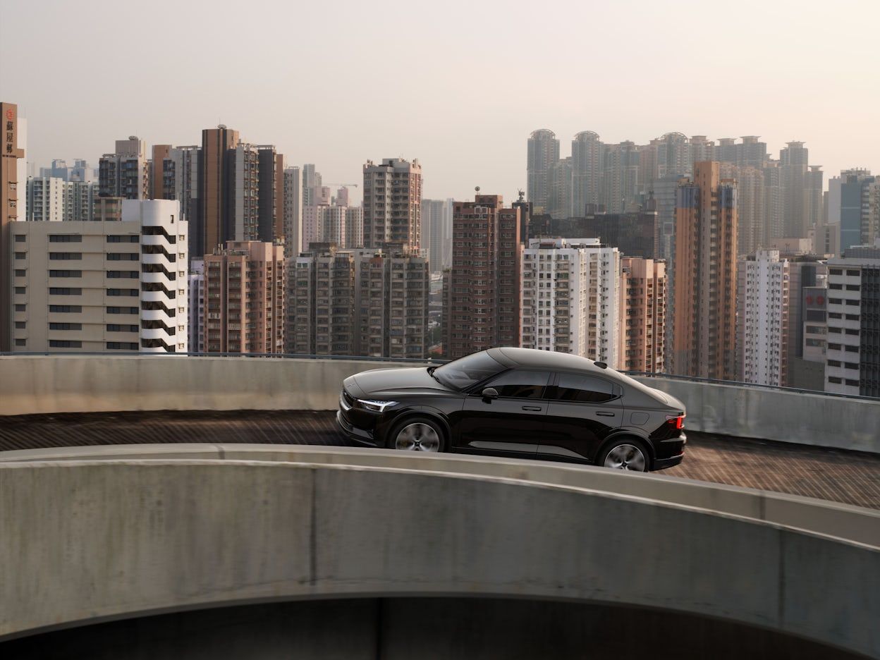 A black Polestar 2 on a road with tall buildings in the background.
