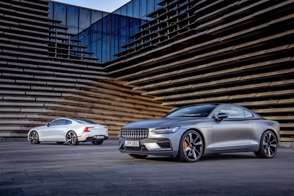 Two Polestar 1, one grey and one white, photographed outside a modern wooden building.