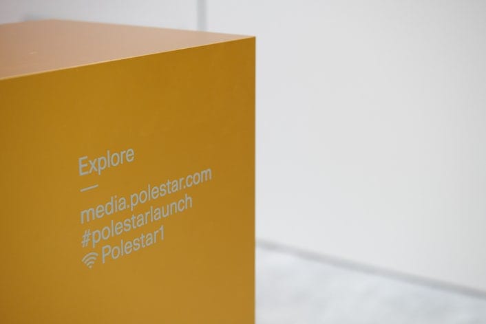 A yellow  sign that reads Explore - media.polestar.com #polestarlaunch Polestar1 and the wifi-symbol