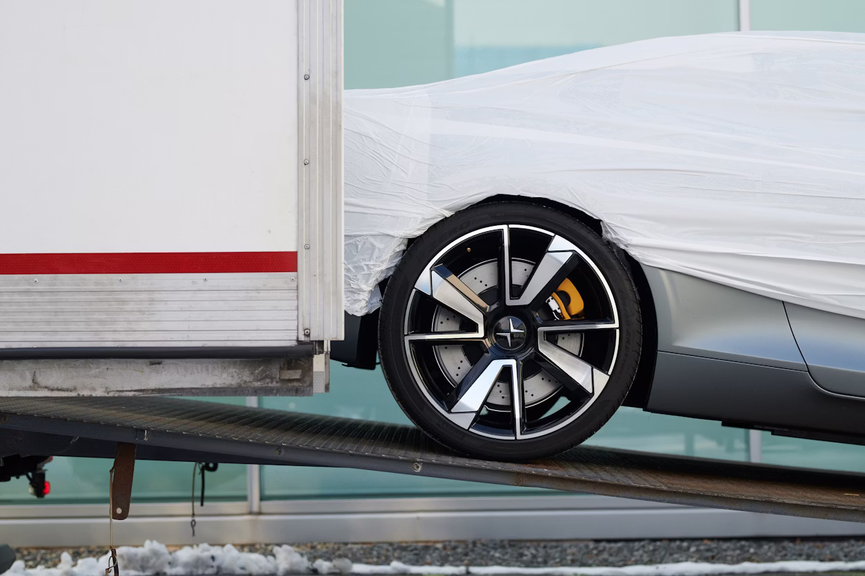 A Polestar 1 covered in white protective plastic being rolled out of a truck.