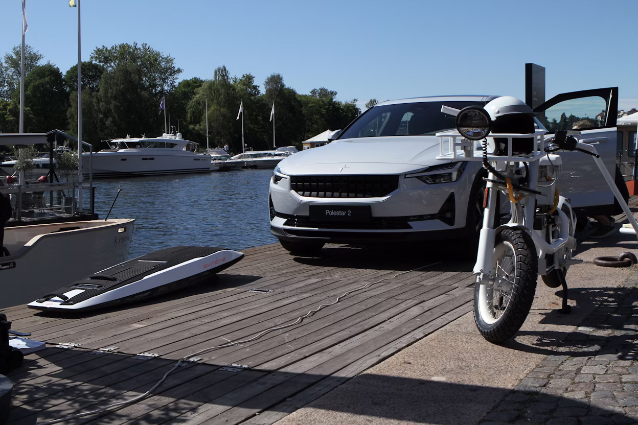 An electric motorbike and a Polestar 2 parked beside a canal.