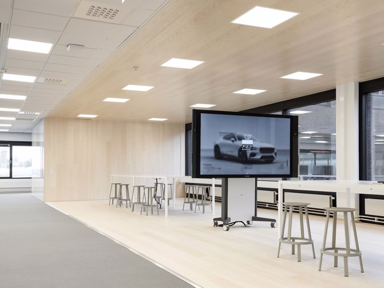 Office interior with white tables, grey chairs and a large screen.