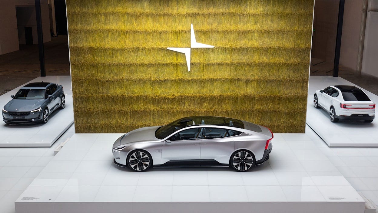 A silver Polestar in front of a gold wall with the Polestar logo