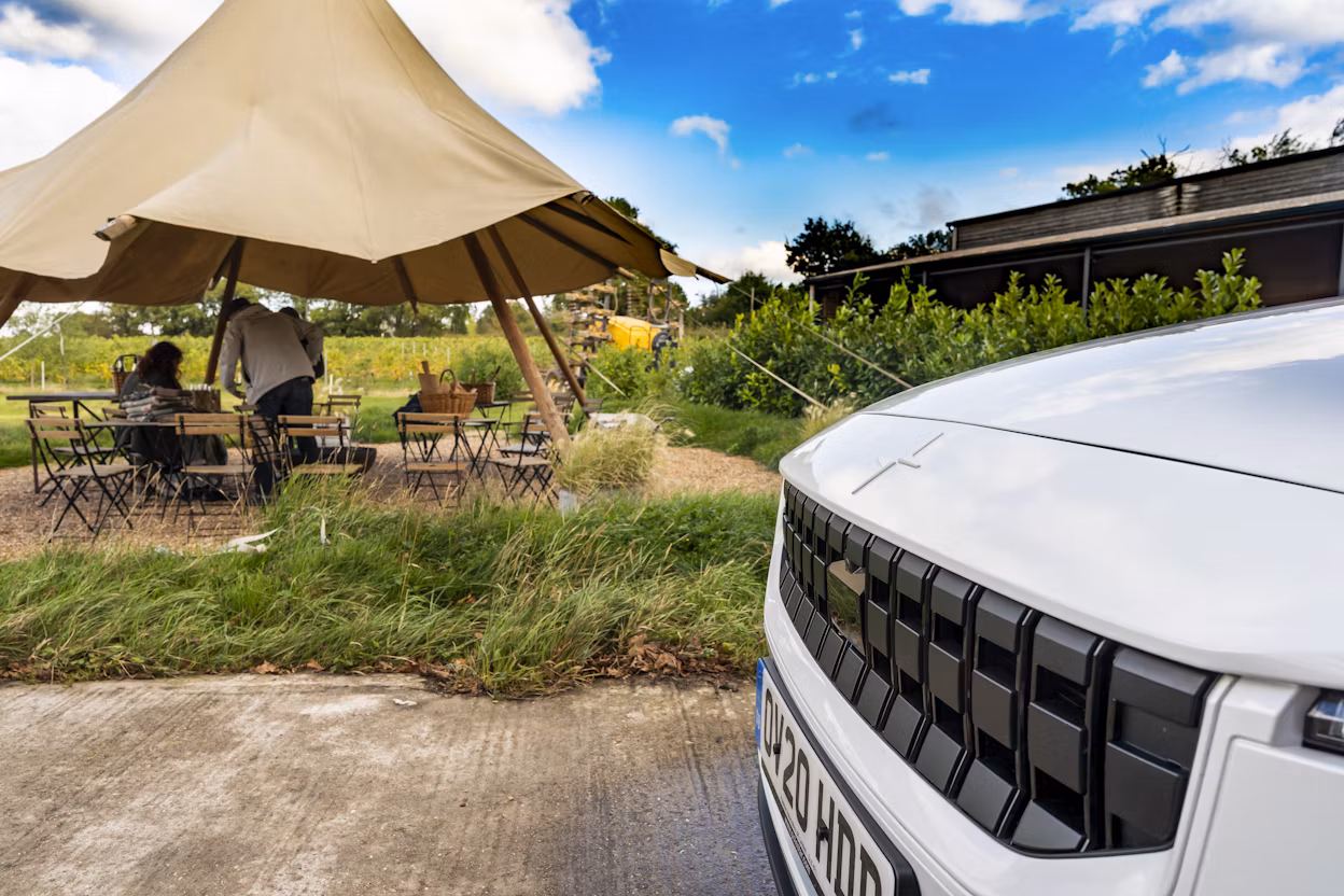 The front of a white Polestar 2 and a tent with tables and chairs visible in the background.