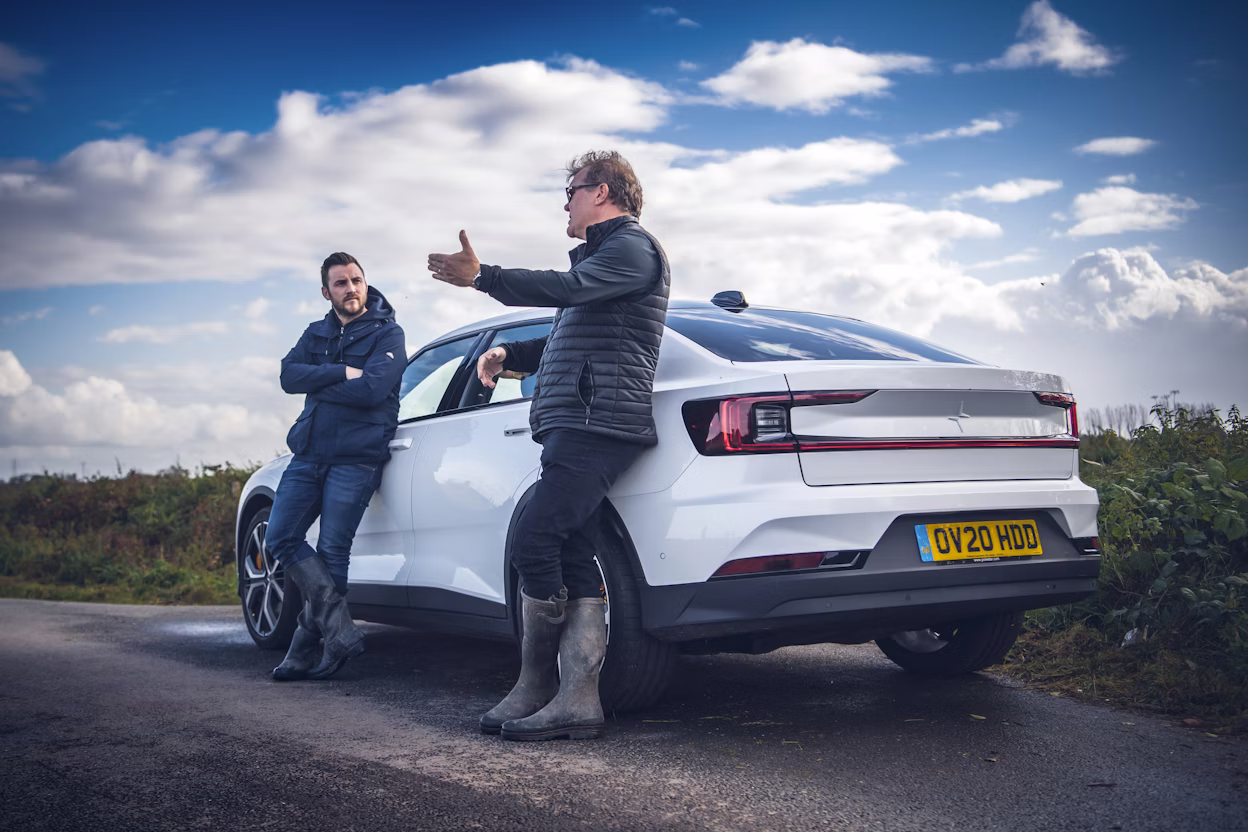 Kirk and Nigel Haworth leaning against a white Polestar 2 parked on the road.