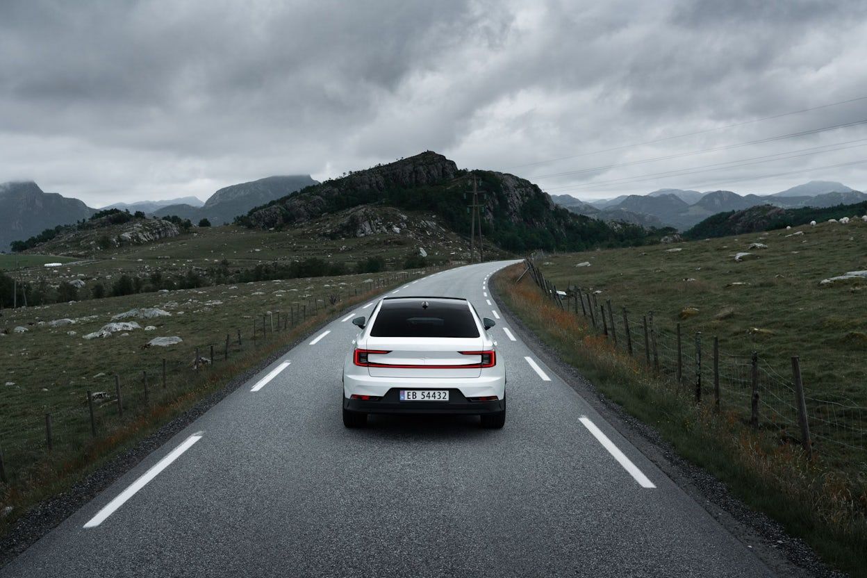 Polestar 2 in white driving on a road with mountains in the background on a cloudy day