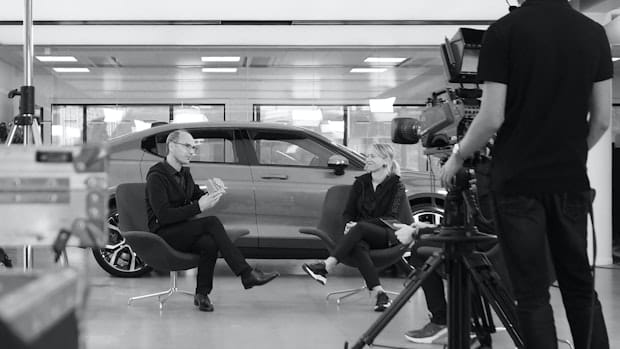 Hans Pehrson and Beatrice Simonsson sitting next to a Polestar while being filmed by a camera man.
