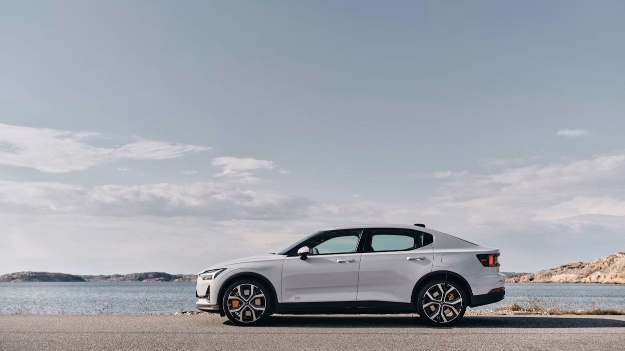 Side view of a white Polestar 2 parked by the ocean.