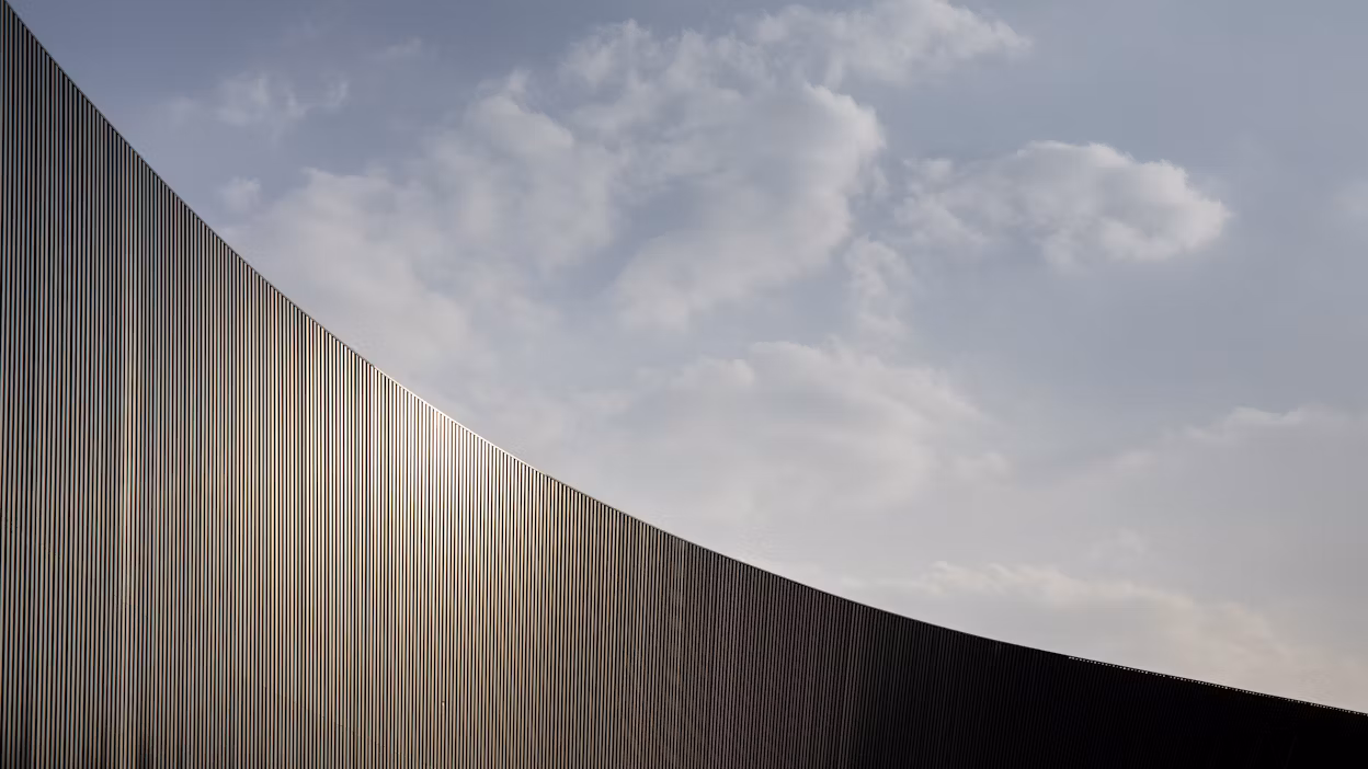 A curved panelled wall with a cloudy sky.