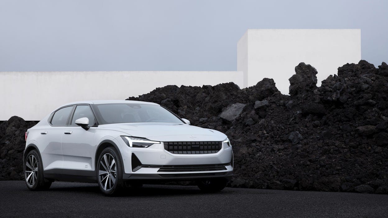 A white Polestar 2 parked next to a stone cairn with black stones.