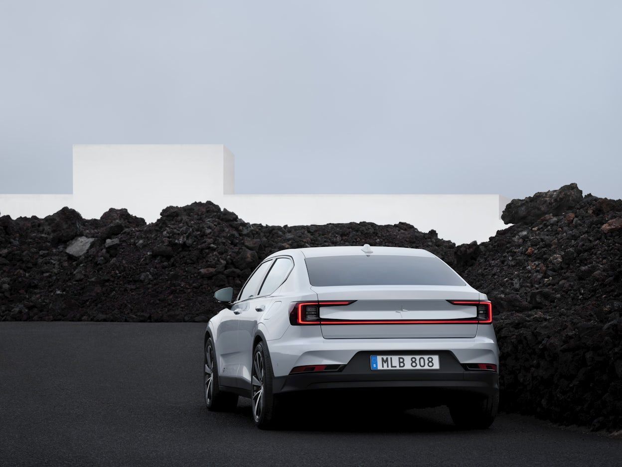 Back view of a white Polestar 2 parked next to a stone cairn with black stones.
