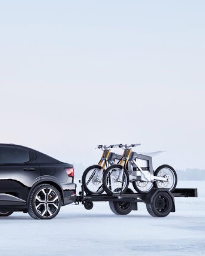 Black Polestar 2 with a trailer with two motorcycles on in winter landscape