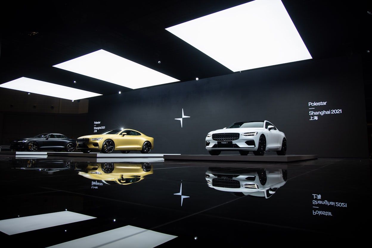 Black, gold, and white Polestar 1 cars lined up in a dark room with white spotlights, at the Auto Shanghai show.