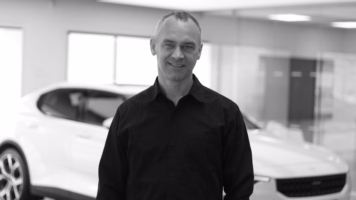 Smiling Christian Appelt standing in front of a white Polestar 2 in a Polestar space.
