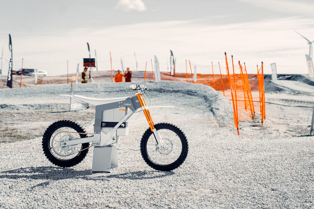 Cake mountain bike displayed on gravel with an orange safety net in the background.