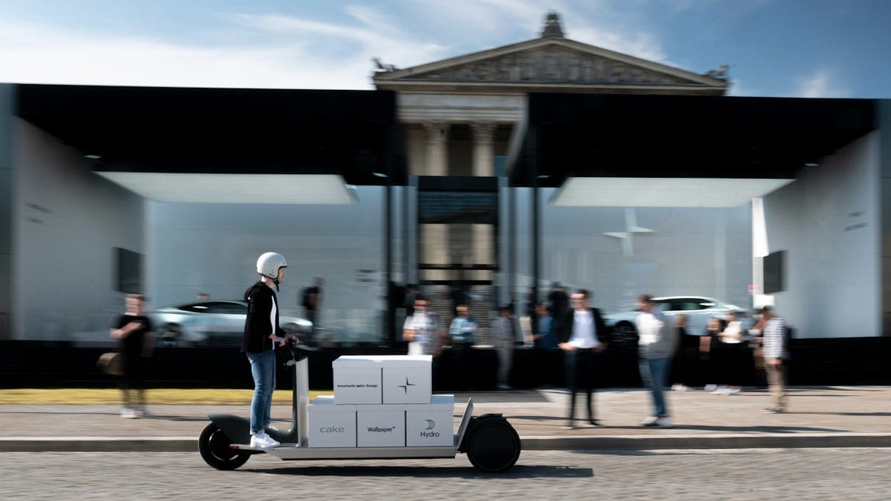 Man riding a scooter with boxes attached to it, with a blurry Polestar space in the background.