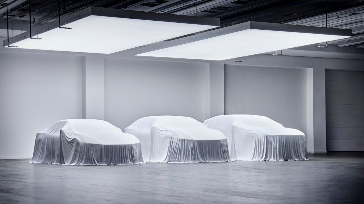 Three Polestar cars covered with white cloths in a showroom.