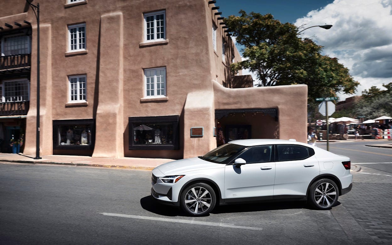 A white Polestar 2 on the road next to a beige building in Santa Fe.
