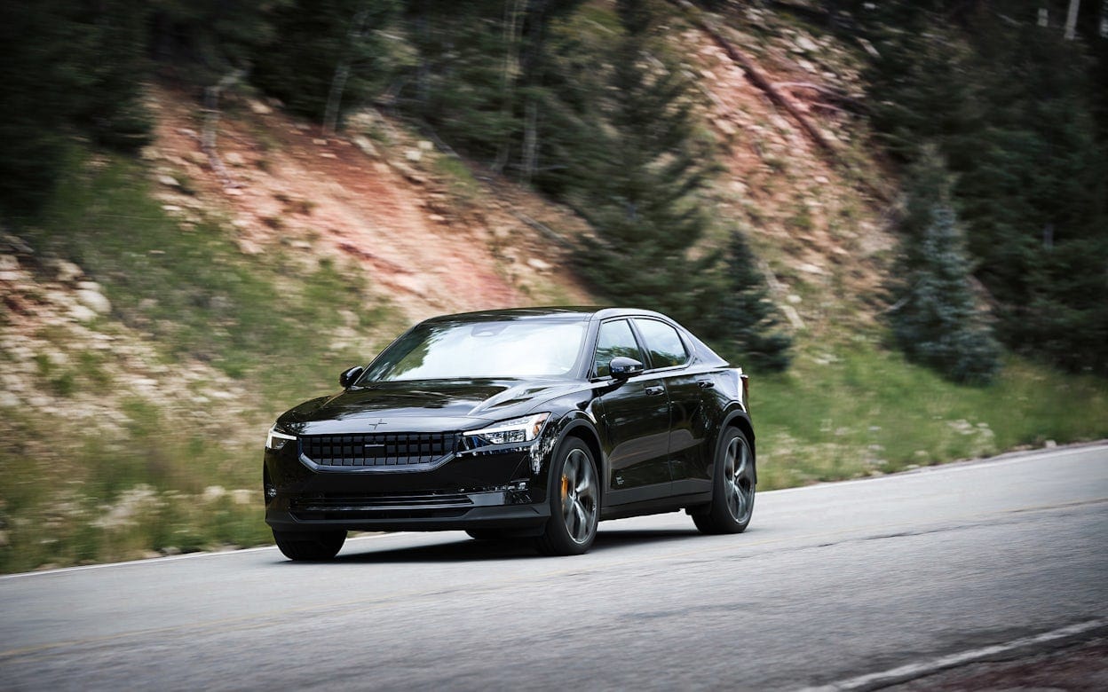 Front view of a black Polestar 2 on a forest road with a blurry background.