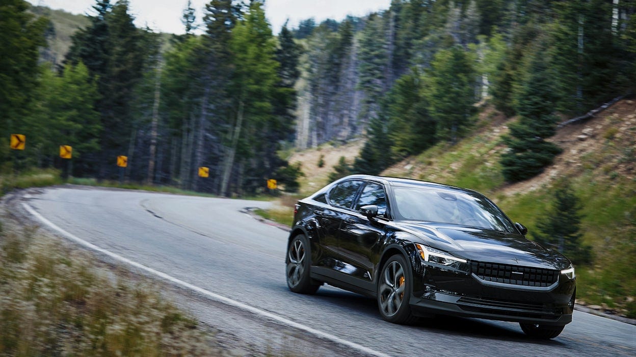 Black Polestar 2 on the road amidst green nature.