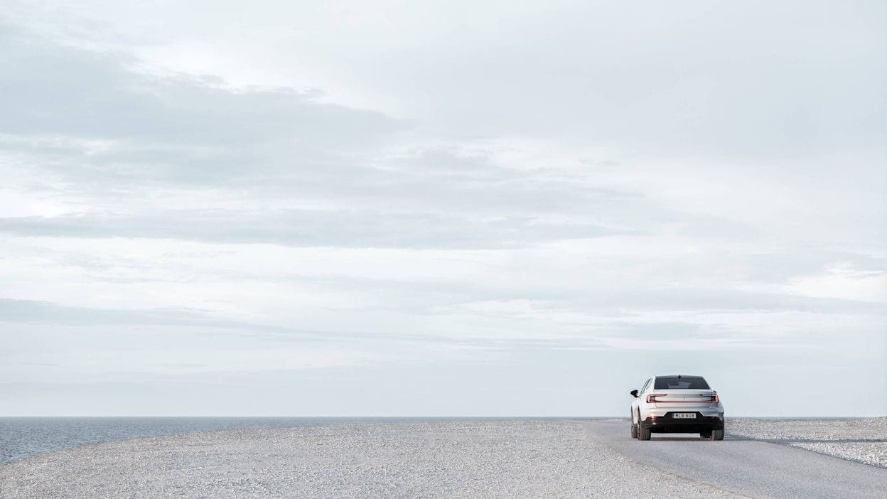 Back view of a white Polestar 2 on a grey road and cloud covered sky above