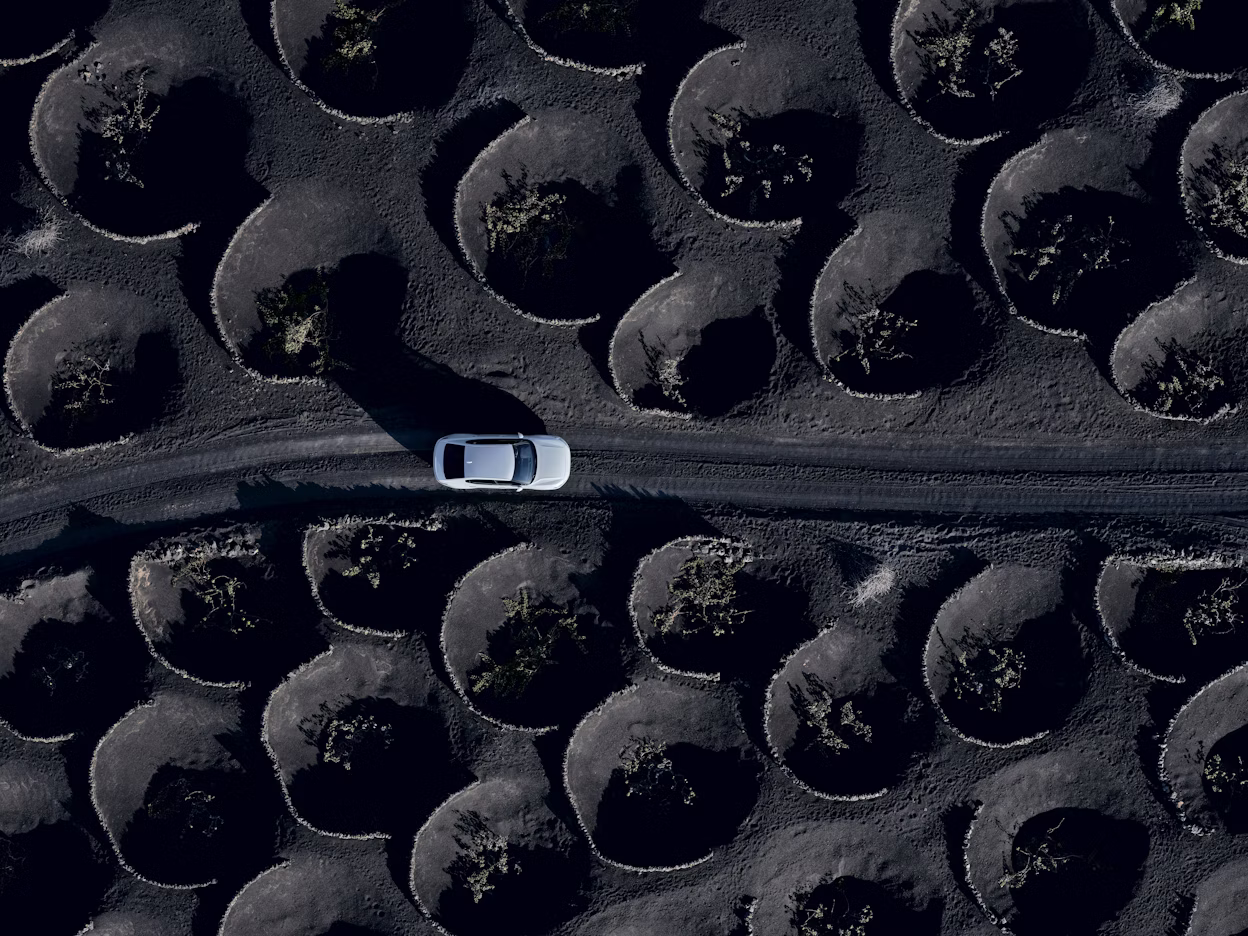 Aerial view of a white Polestar 2 on the road with black nature around.