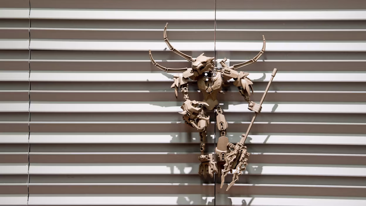 Art piece resembling a robot made out beige plastic attached to a metallic wall.