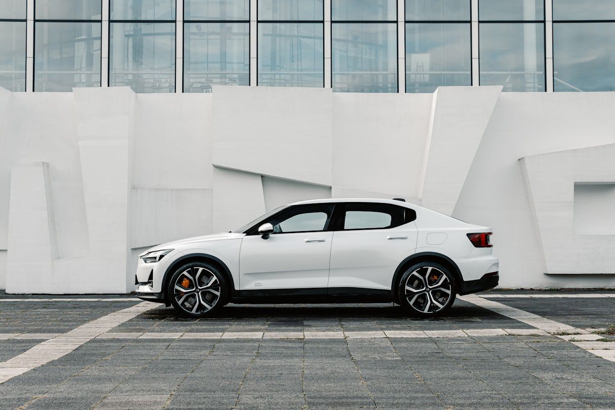 Side view of a white Polestar 2 on the parking lot next to a building.