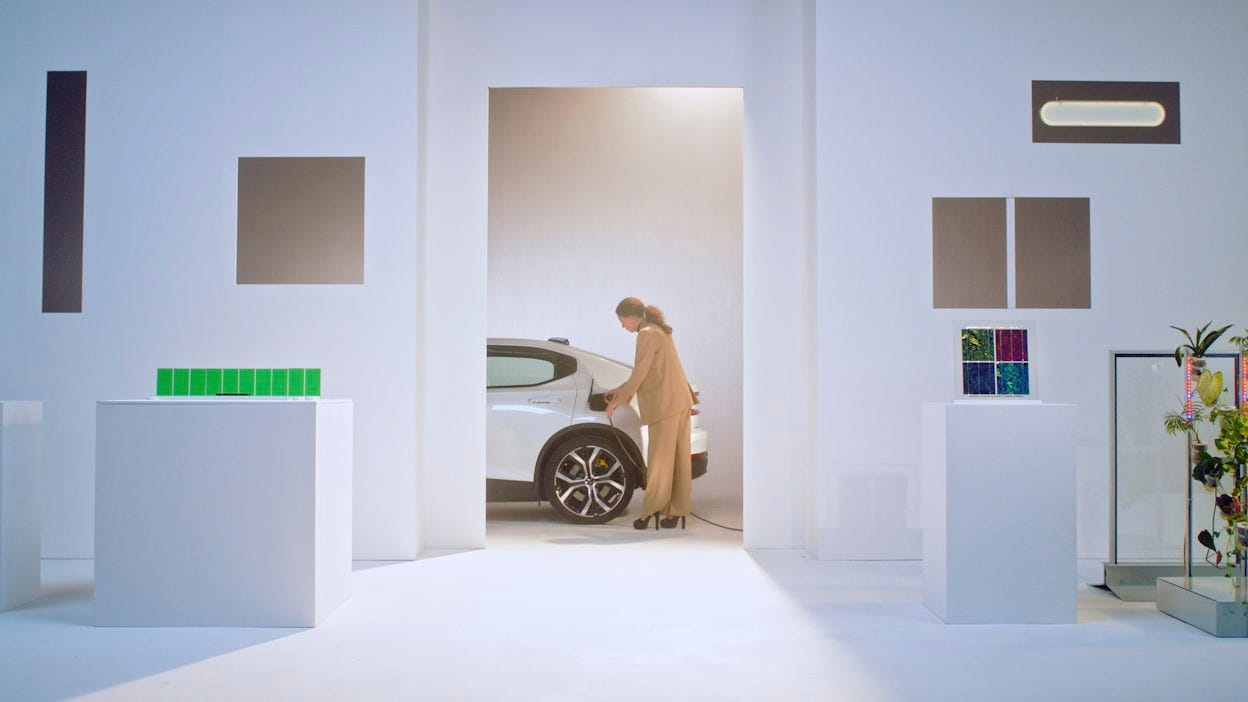 Woman standing next to a Polestar and plugging in the charger.