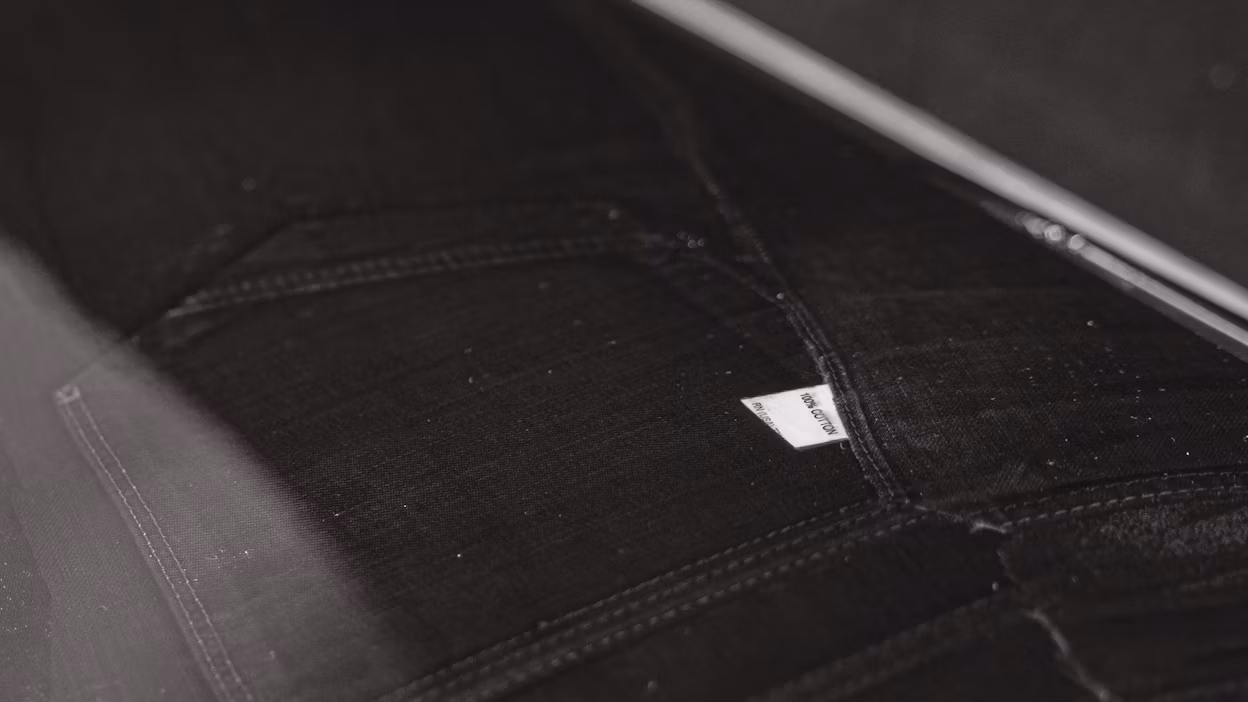 Close-up of dark fabric with stitching and a small visible label reading "Iron Cotton".