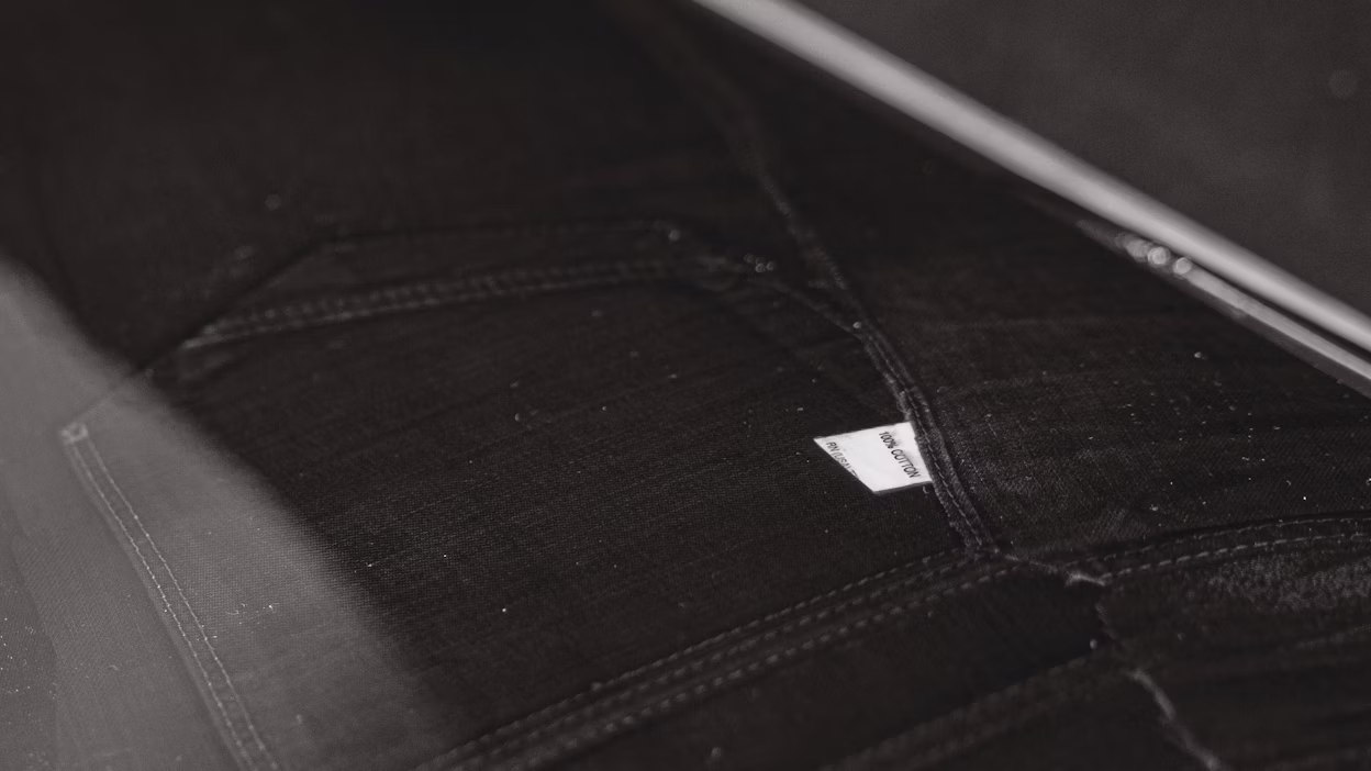 Close-up of dark fabric with stitching and a small visible label reading "Iron Cotton".