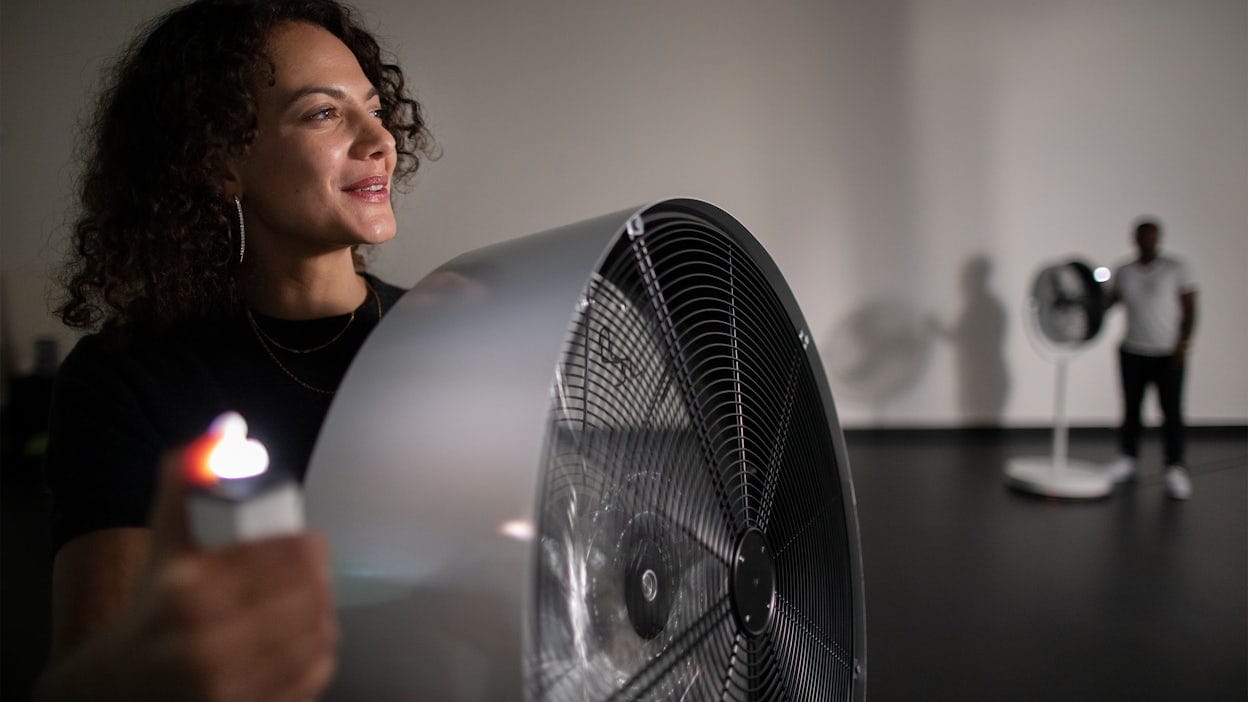Visitors at an art exhibition use fans to control the wind.