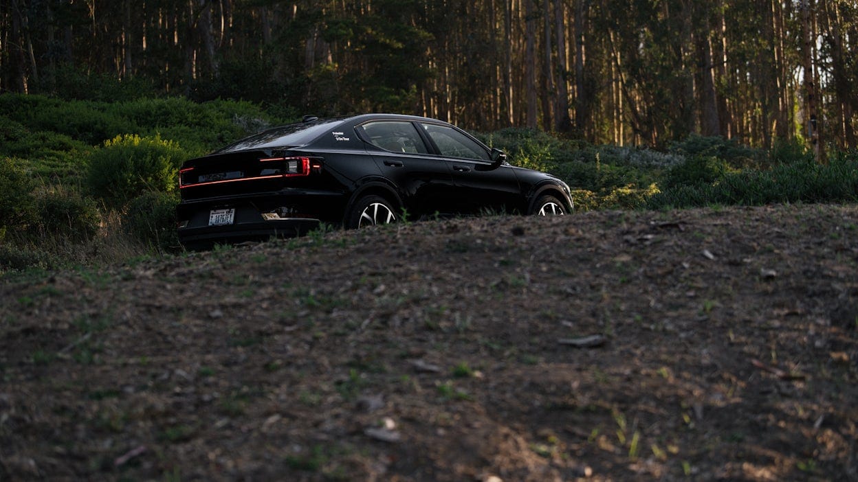 Black Polestar 2 driving on the road in a lush forest.
