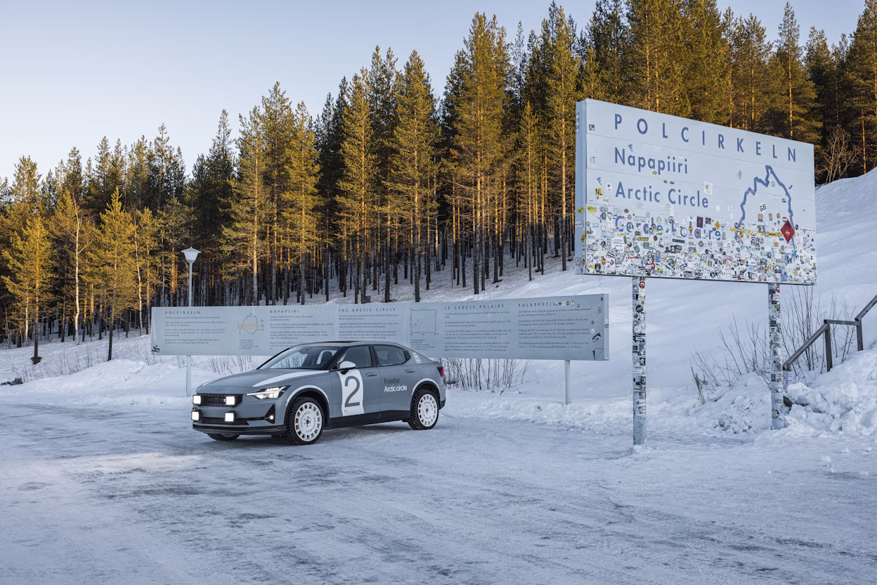 Side view of a grey Polestar 2 parked next to a sign saying Polcirkeln, Napapiiri, Arctic Circle.