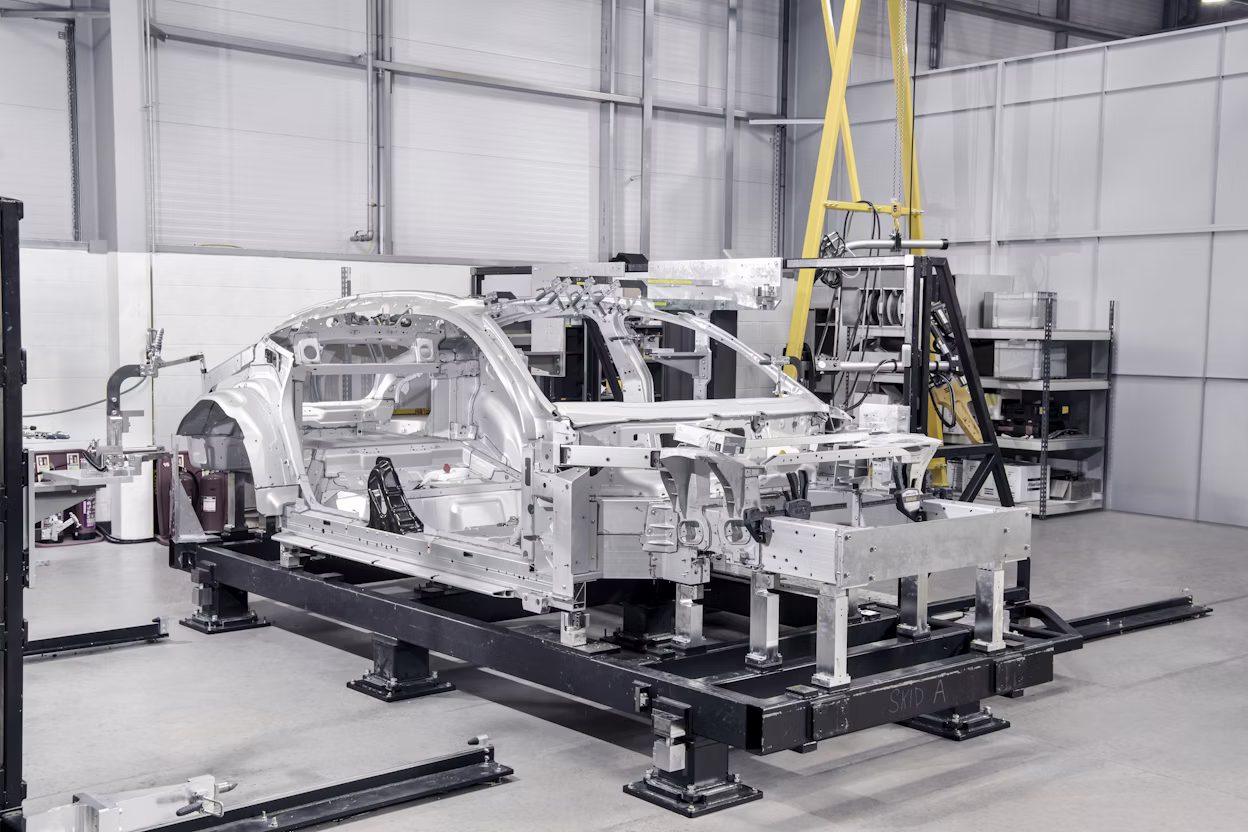 Polestar car frame on assembly rig in an industrial facility with tools, shelves, and equipment in the background.