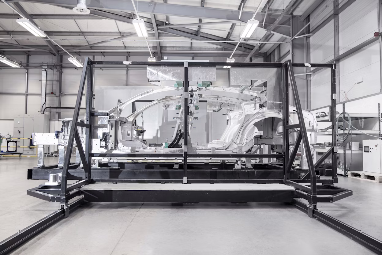Automotive assembly area with a metal frame holding a partially assembled Polestar car chassis in a factory setting.