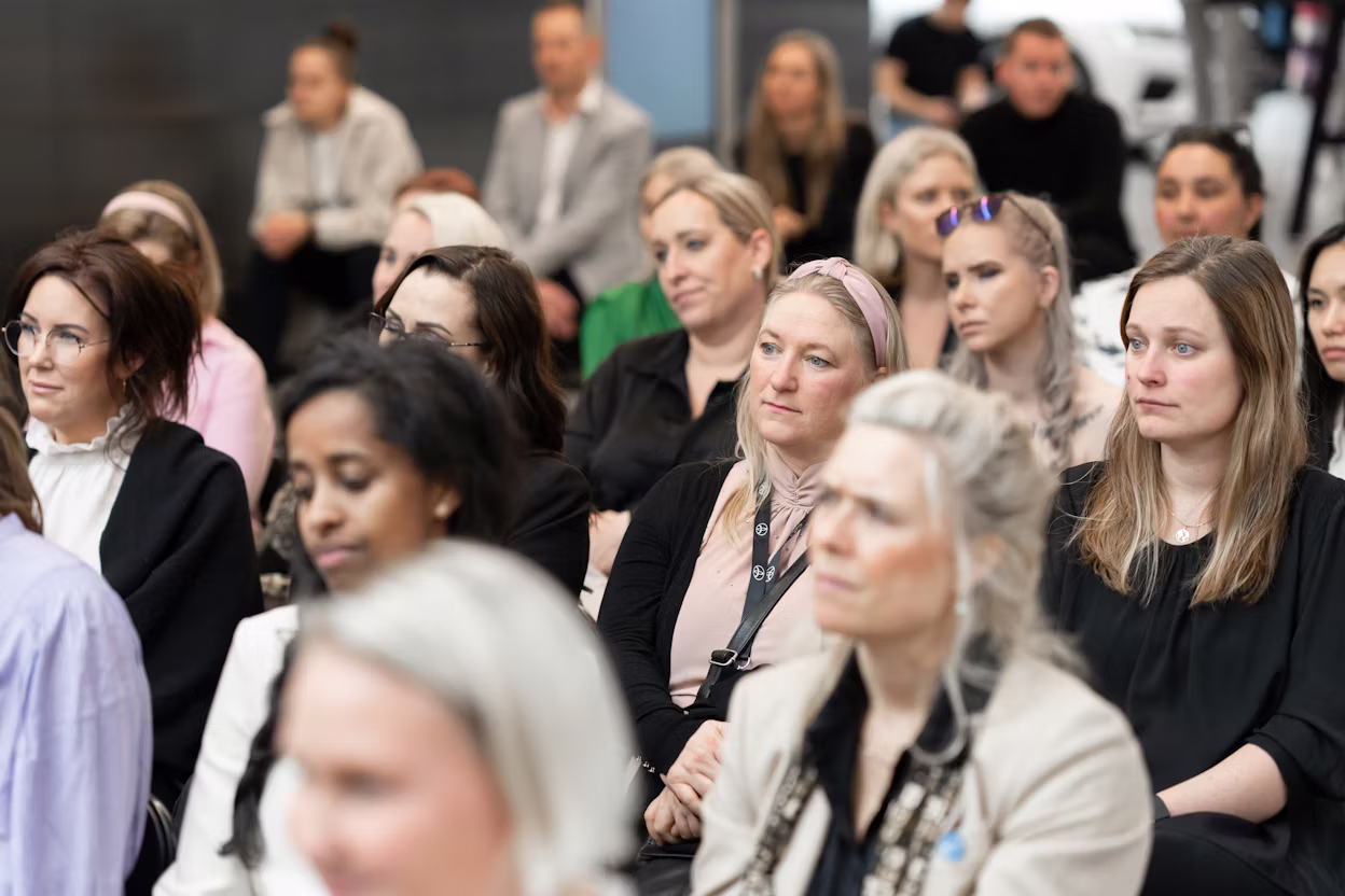 People seated indoors with blurred faces, a Polestar car visible in the background.
