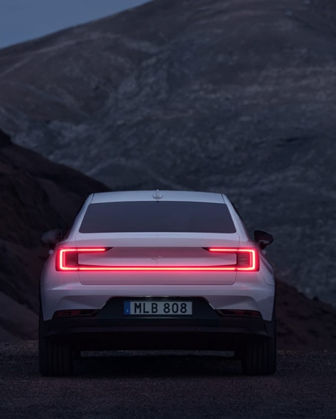 Backfront of White Polestar 2 with taillights on in mountain landscape