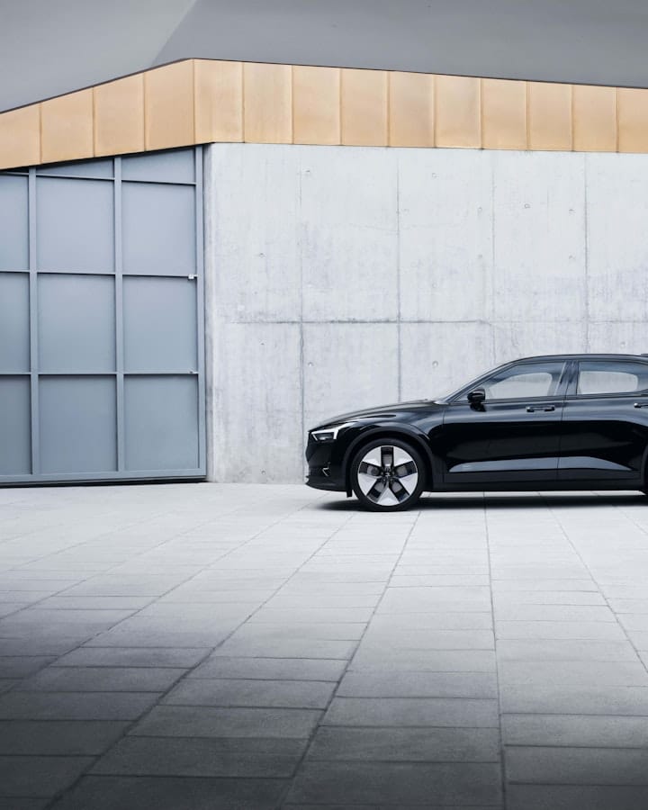 Image of a black Polestar 2 in front of a grey building. 