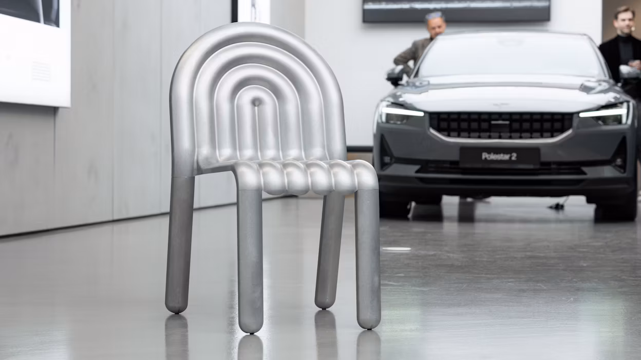 Image of an aluminium chair in front of a Polestar 2.