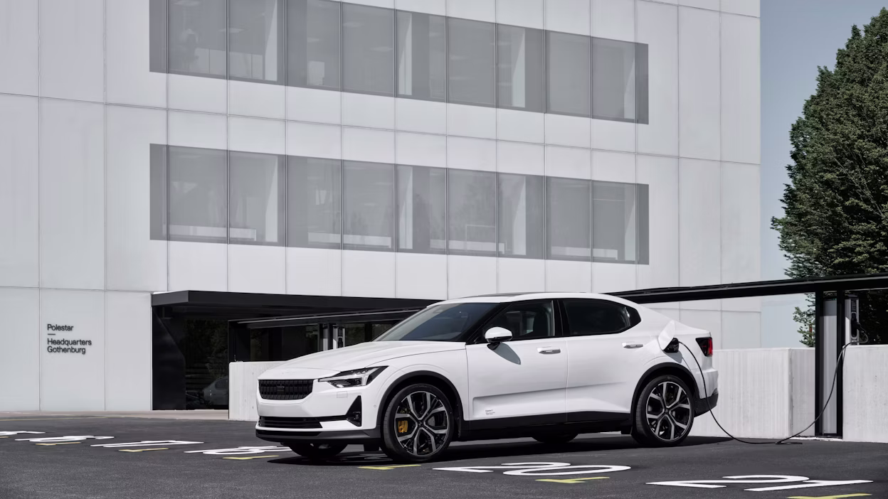 Image of a white Polestar 2 charging in front of white building.