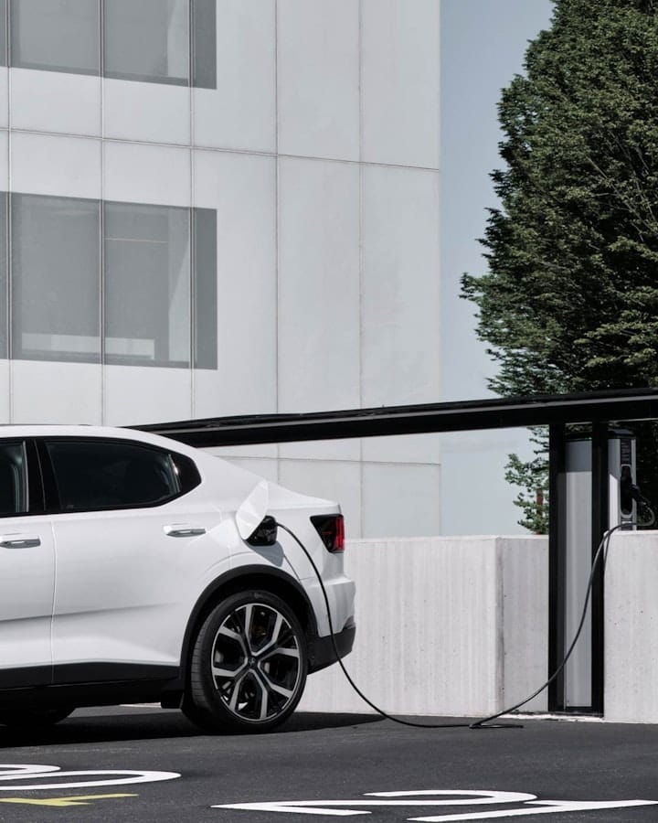 Image of a white Polestar 2 charging in front of white building. 