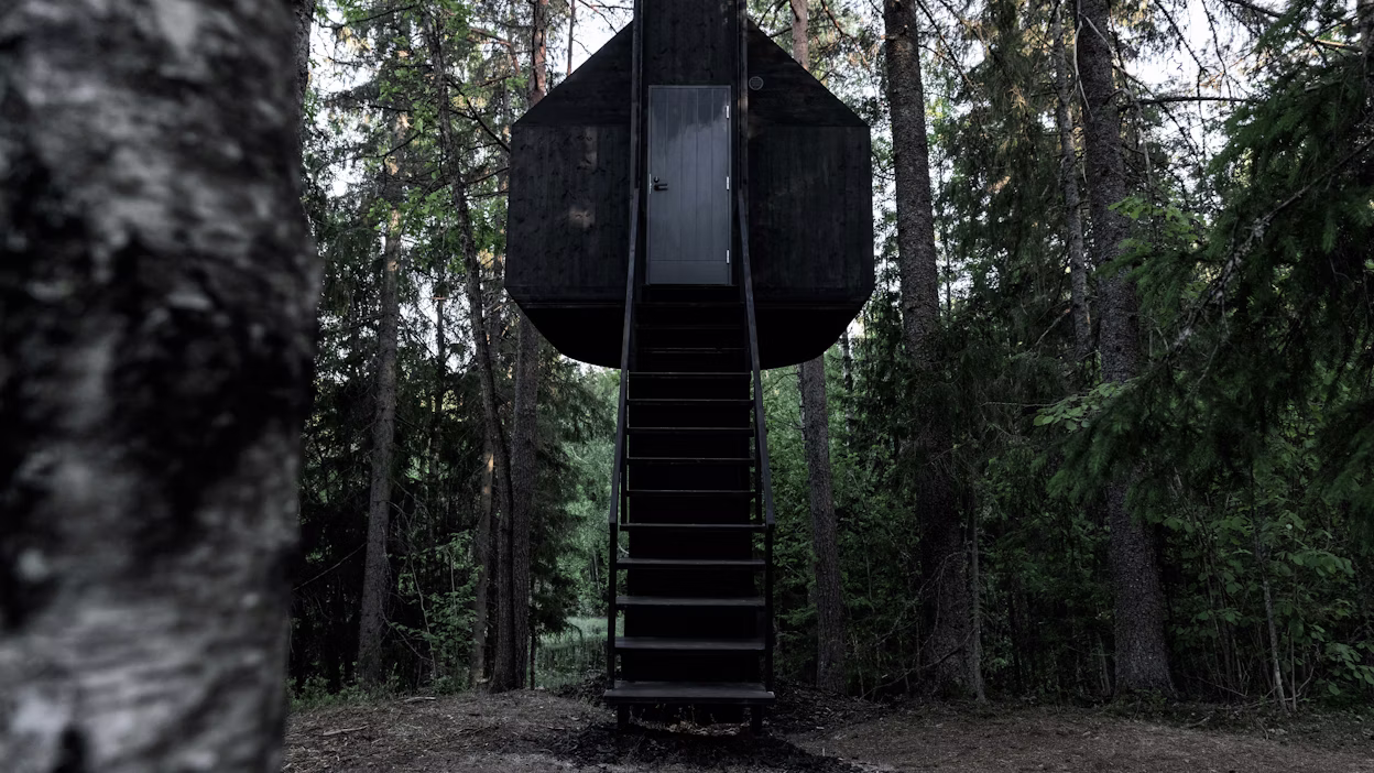 A black treehouse with stairs leading up to it.