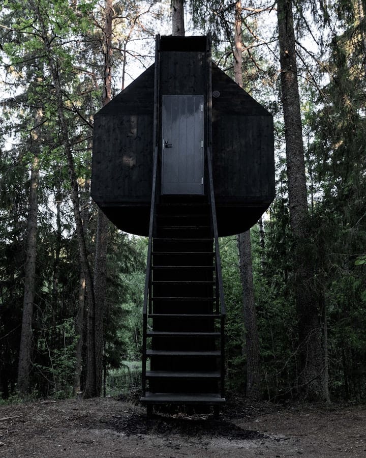 A black treehouse with stairs leading up to it. 