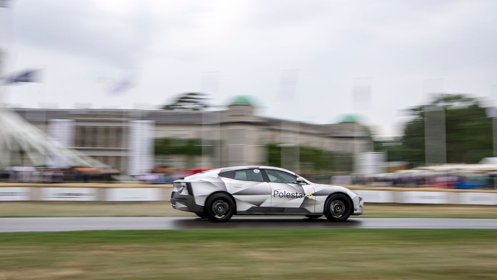 A camouflaged Polestar 5 prototype moving at speed up The Hillclimb with a blurred background. 