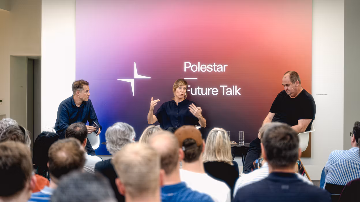 Audience attending Polestar Future Talk event with three speakers seated on stage in front of a gradient backdrop.
