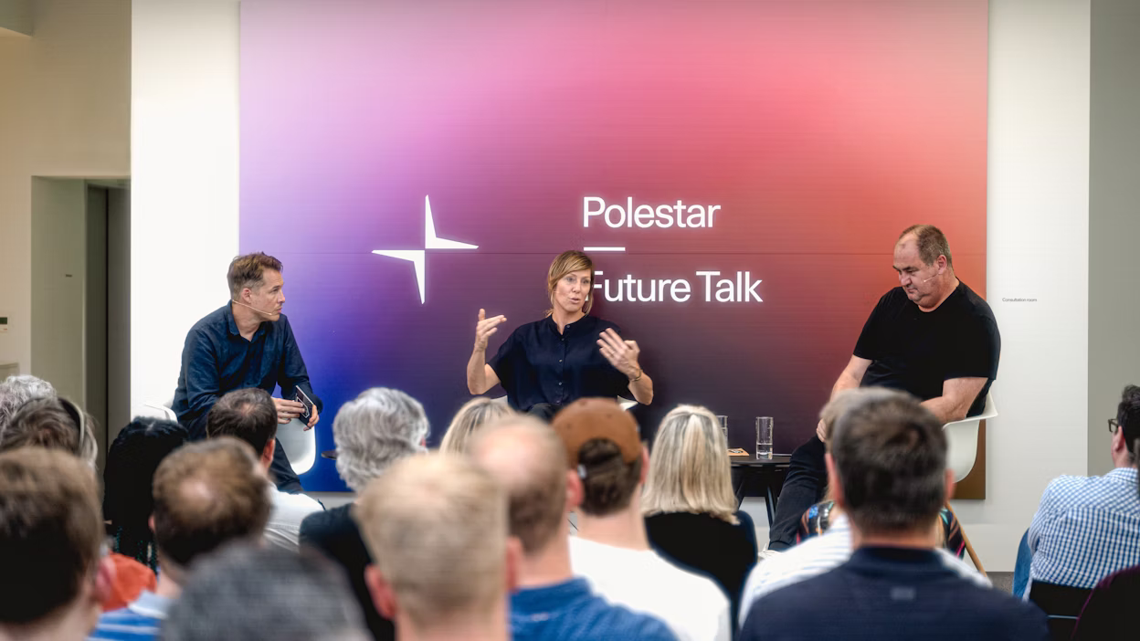 Audience attending Polestar Future Talk event with three speakers seated on stage in front of a gradient backdrop.