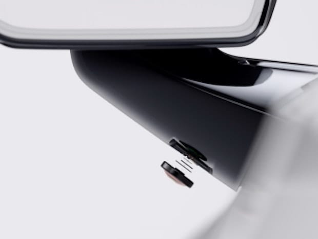 Close up shot showing the bottom fixture connectiong the frameless side mirror to the Polestar 2 electric vehicle. On the fixture is a small driver safety sensor, which has been deconstructed to show it's internal workings.